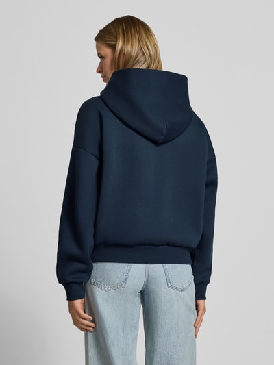 Frauenmodel trägt Kapuzenpullover aus Baumwoll-Mix von REVIEW in Dunkelblau mit lockerer Passform, gerippten Bündchen, Känguru-Tasche, Ganzkörperansicht Rückansicht.