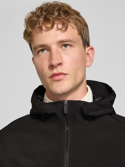 Männermodel trägt Regular Fit Jacke mit Kapuze Modell 'Charge' von JACK & JONES in Schwarz, glatte Struktur, Nahaufnahme Oberkörper. Damen Jacke mit Reißverschluss, Rückenlänge 68 cm, Schulterbreite 50 cm, Brustweite 60 cm, Ärmellänge 66 cm.