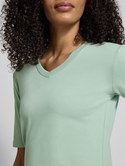Kobiece model prezentuje T-shirt mit V-Ausschnitt od Christian Berg Woman, mieszanka bawełny i elastanu, krój regular fit, rękaw o dł. 1/2, długość tyłu w rozmiarze S: 55 cm, jasna zieleń, gładka faktura, zbliżenie na górną część ciała