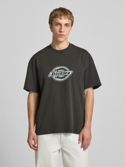 Männermodel trägt Herren T-Shirt mit Logo-Print Modell 'PLAINVILLE' von Dickies aus Reine Baumwolle in Schwarz, Relaxed-Fit, Ganzkörperansicht von vorne. Rückenlänge bei Größe M: 69 cm.