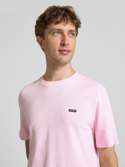 Männermodel trägt T-Shirt mit Label-Patch und Rundhalsausschnitt von REVIEW, Reine Baumwolle, Boxy-Fit, zartrosa, Nahaufnahme Oberkörper.