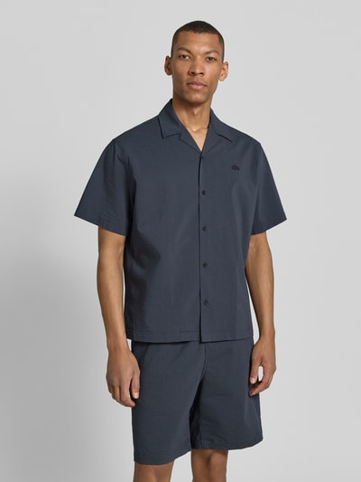Męski model nosi Relaxed Fit Freizeithemd aus reiner Baumwolle od Lacoste, kratki rękaw, denim, resortowy kołnierz, materiał crinkle, całościowy frontowy widok