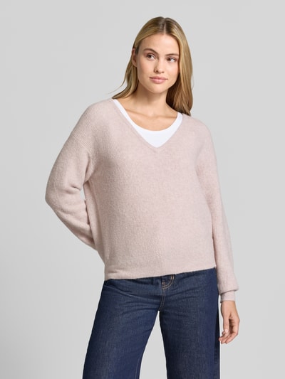 Modelka nosi sweter z dzianiny z mieszanki materiałów z lnem, model 'DAMSVILLE' od American Vintage, efekt prążkowania, dekolt w serek, elastyczne wykończenia, długość tyłu w rozmiarze XS/S 61 cm, długość rękawów 54 cm, jasny róż, luźny krój, widoczne tekstury dzianiny, widok całej sylwetki z przodu.