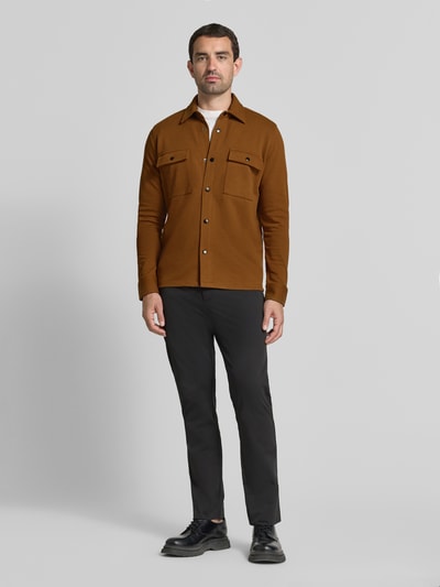 Männermodel trägt Relaxed Fit Freizeithemd aus Baumwoll-Mix Modell 'JACKIE' von Selected Homme in Braun, kombiniert mit schwarzer Hose, Ganzkörperansicht von vorne. Herren Freizeithemd von Selected Homme.