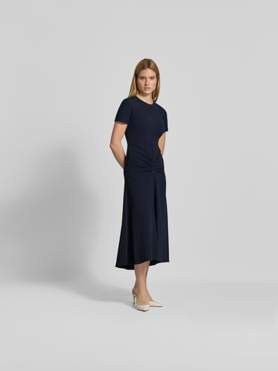 Frauenmodel trägt Midikleid aus Viskose-Mix von Victoria Beckham in Dunkelblau mit Rundhalsausschnitt, kurzen Ärmeln, taillierter Passform und Raffungen, glatte Textur, Ganzkörperansicht von vorne.