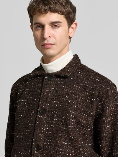 Mężczyzna nosi Relaxed Fit Jacke mit Baumwoll-Anteil von Forét, materiał bouclé, brązowa z czarnymi i białymi nićmi, zapięcie na guziki, kołnierz, mix materiałów, zdjęcie z przodu, zbliżenie na górną część ciała.