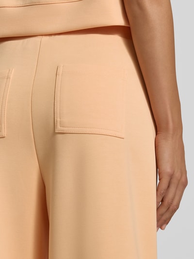 Frauenmodel trägt Wide Leg Sweatpants aus Modal-Mix von Rich & Royal in Pfirsichfarbe mit elastischem Bund, Bundfalten und Gesäßtaschen, Detailaufnahme Rückansicht.
