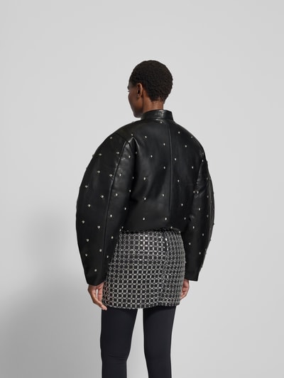 Frauenmodel trägt Jacke mit Stehkragen von ROTATE, schwarze Leder-Optik, Ziersteinbesatz, Reißverschluss, Ganzkörperansicht Rückansicht. Rückenlänge 57 cm, Brustweite 51 cm, Ärmellänge 65 cm bei Größe 36.