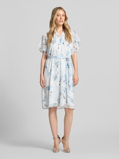 Frauenmodel trägt Knielanges Kleid mit Serafino-Kragen von More & More aus Chiffon, Taillierter Schnitt, Schmetterlingsärmel, Bindegürtel, Ganzkörperansicht von vorne.