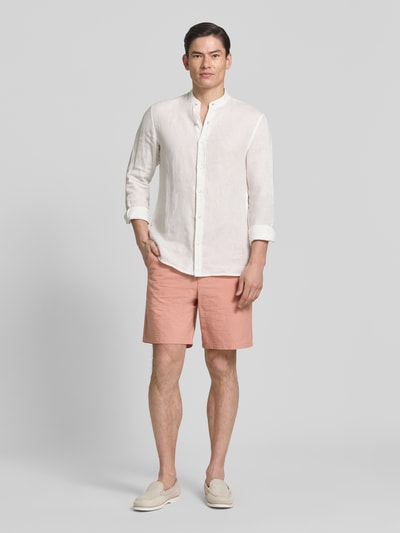 Męski model nosi Regular Fit Bermudas aus Baumwoll-Mix Modell 'KARL' od SELECTED HOMME, brzoskwiniowy kolor, długość nad kolano, materiał seersucker, kieszenie boczne i tylne, gładka tekstura, widok całej sylwetki z przodu.