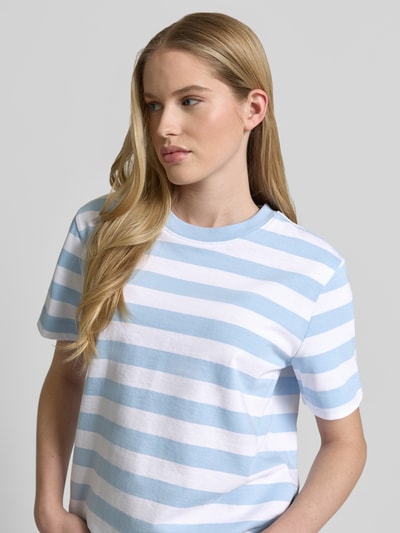 Modelka nosi damski t-shirt Boxy Fit T-Shirt aus reiner Baumwolle Modell 'ESSENTIAL' od Selected Femme, efekt: wzór w paski, okrągły dekolt, krótki rękaw, wykończenie materiału: heavy dżersej, materiał: czysta bawełna, kolor biało-niebieski, naszywka z logo, półzbliżenie od przodu.
