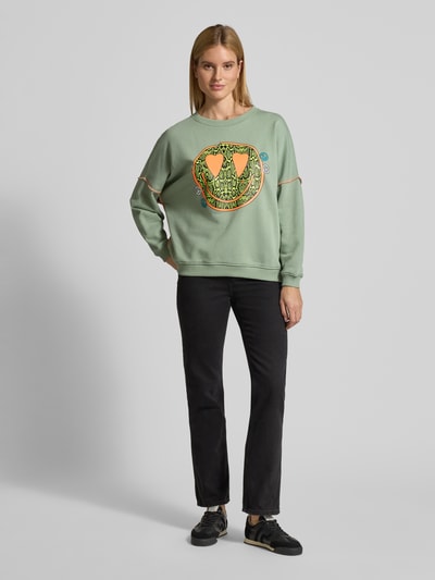 Frauenmodel trägt Oversized Sweatshirt mit Motiv-Print Modell 'Heartface' von miss goodlife in Hellgrün mit elastischen Abschlüssen, aus reiner Baumwolle, Ganzkörperansicht von vorne.