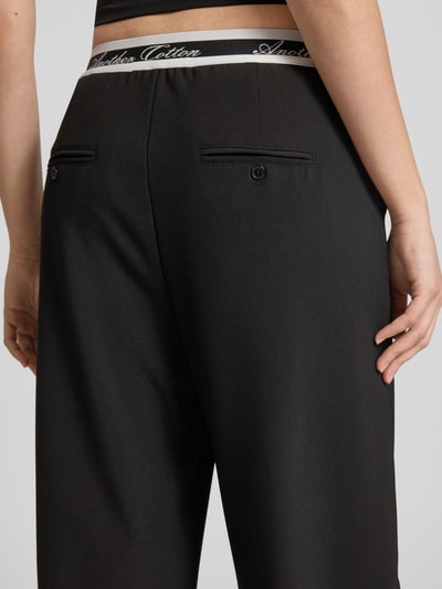 Männermodel trägt Wide Leg Hose mit elastischem Logo-Bund von ANOTHER COTTON LAB, mieszanka materiałów z dodatkiem streczu, wpuszczane kieszenie, szerokość w rozmiarze S: 36 cm, długość wewnętrzna nogawki w rozmiarze S: 75 cm, kolor czarny, gładka faktura, detailaufnahme tyłu.