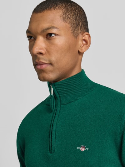 Männermodel trägt Pullover aus reiner Wolle von GANT in Grün, hochgeschlossener Troyer-Kragen, Reißverschluss, Feinstrick, Nahaufnahme Oberkörper.