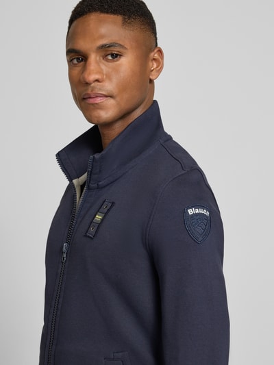 Männermodel trägt Sweatjacke mit Stehkragen Modell 'City New' von Blauer Usa in dunkelblauem Baumwoll-Mix, Label-Detail, Slim-Fit, Nahaufnahme Oberkörper. Rückenlänge bei Größe M: 45 cm, Ärmellänge bei Größe M: 84 cm.
