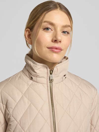 Kobiece modelka nosi Steppjacke mit Zweiwege-Reißverschluss od Fuchs Schmitt w kolorze beżowym, krój regular fit, stójka, kaptur, wpuszczane kieszenie, długość tyłu w rozmiarze 36: 60 cm, szerokość ramion w rozmiarze 36: 41 cm, szerokość klatki piersiowej w rozmiarze 36: 47 cm, długość rękawów w rozmiarze 36: 63 cm, zamek błyskawiczny dwustronny, pikowana faktura, zbliżenie na górną część ciała