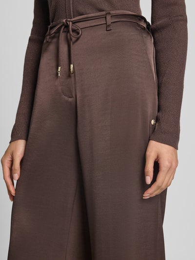 Frauenmodel trägt schimmernde Wide Fit Hose mit Bindegürtel von Marc Cain, High Waist, braune Farbe, Detailaufnahme, Nahaufnahme Oberkörper.