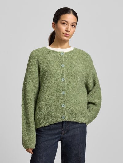 Frauenmodel trägt locker geschnittene, grüne Strickjacke mit Knopfleiste Modell 'ZOLLY' von American Vintage, Rundhalsausschnitt, gerippte Abschlüsse, Lanawoll-Alpaka-Mix, Nahaufnahme Oberkörper.