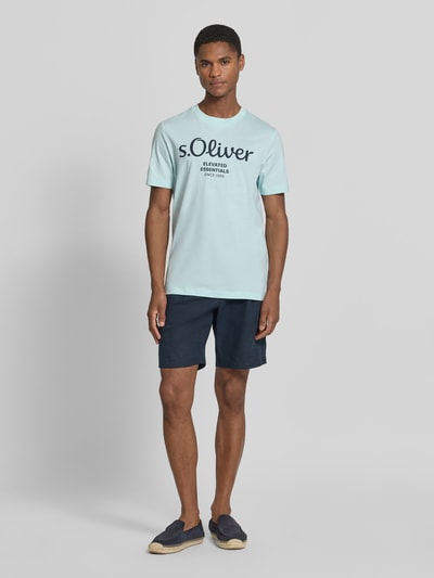 Męski model nosi Regular Fit T-Shirt aus reiner Baumwolle von s.Oliver RED LABEL, efekt: jednolity kolor, krój regular fit, nadruk z logo, okrągły dekolt, krótki rękaw, dżersej, czysta bawełna, całkowity widok z przodu.