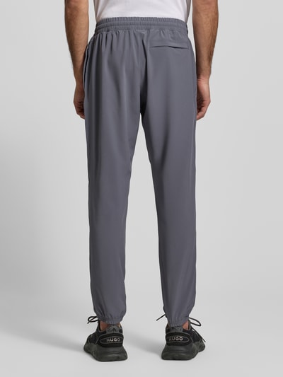 Männermodel trägt Regular Fit Jogger mit Logo-Print Modell 'Vibe' von Under Armour in Grau, Elastischer-Material-Mix, Eingrifftaschen, Rückansicht Ganzkörperansicht