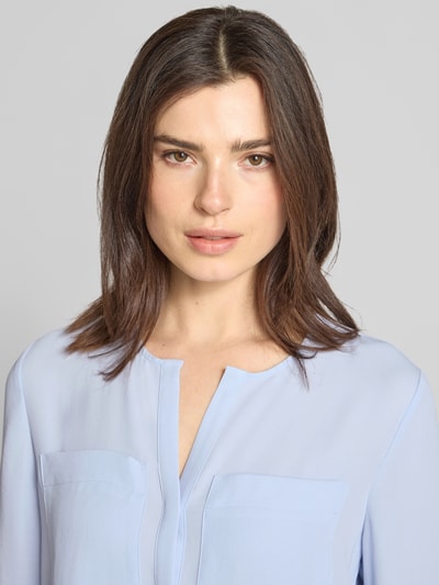Frauenmodel trägt Regular Fit Bluse mit Brusttaschen von Marc Cain, tunika-Ausschnitt, hellblau, glatte Textur, Nahaufnahme Oberkörper.