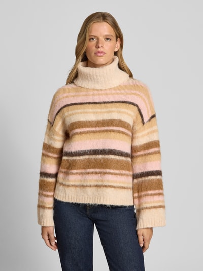 Kobiece modelka nosi Loose Fit Rollkragenpullover mit Woll-Anteil Modell 'PERIL' od ONLY, kremowe tło, pastelowe i brązowe paski, tekstura miękkiej dzianiny, Ganzkörperansicht von vorne, damski golf od ONLY.