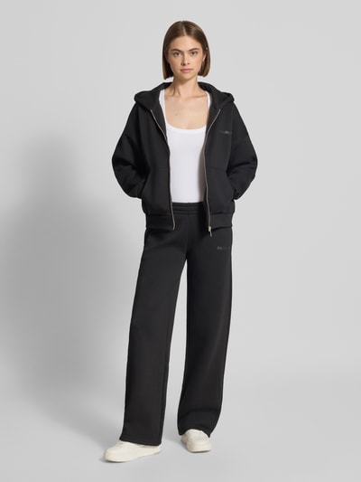 Frauenmodel trägt Straight Fit Sweatpants aus Baumwoll-Mix mit Logo-Print von Review in Schwarz, weiche Textur, Ganzkörperansicht von vorne. Baumwoll-Mix, elastischer Bund, Innenbeinlänge 81 cm bei Größe S.