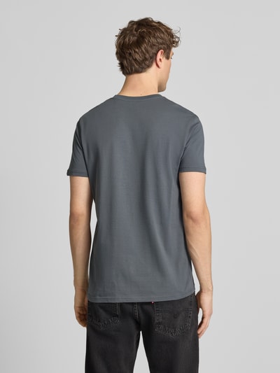 Męski model nosi T-Shirt aus Baumwolle von Alpha Industries, prosty krój, okrągły dekolt, szary, długość tyłu w rozmiarze M: 68 cm, Ganzkörperansicht Rückansicht.