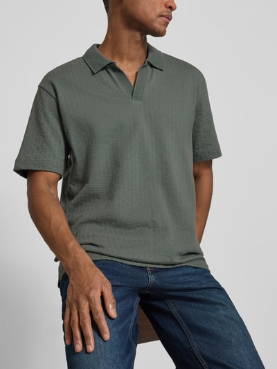Männermodel trägt Relaxed Fit Poloshirt aus reiner Baumwolle von Marc O’Polo in Olivgrün, unifarben, strukturierte Webtextur, Nahaufnahme Oberkörper.