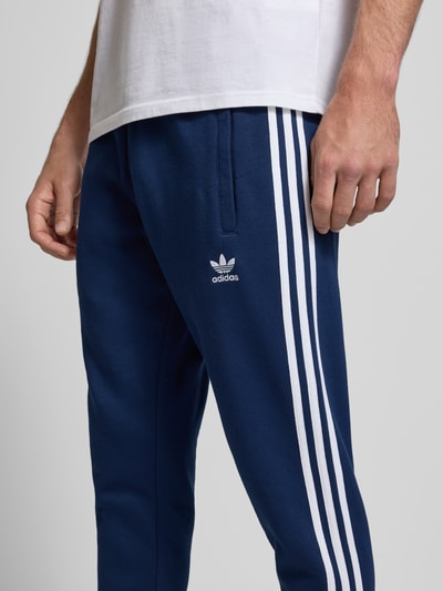 Männermodel trägt Sweatpants mit elastischem Bund von adidas Originals, dunkelblau, Baumwoll-Mix, Eingrifftaschen, Label-Stitching, Nahaufnahme Oberkörper.