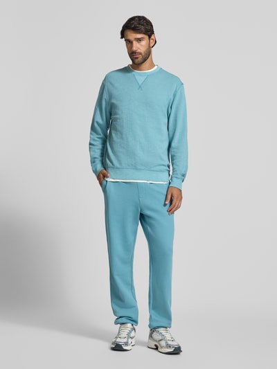 Männermodel trägt Regular Fit Sweatshirt aus Baumwoll-Mix von Scotch & Soda in Hellblau mit Rundhalsausschnitt und elastischen Abschlüssen, Ganzkörperansicht von vorne.