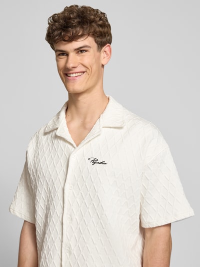 Männermodel trägt Regular Fit Freizeithemd mit Label-Stitching Modell 'Jovren' von Pegador, Weiß, Rautenstruktur, Halbarm, Nahaufnahme Oberkörper. Elastischer-Material-Mix mit Baumwoll-Anteil, Reverskragen, Knopfleiste, Rückenlänge bei Größe M: 72 cm, Schulterbreite: 45 cm, Ärmellänge: 33 cm.