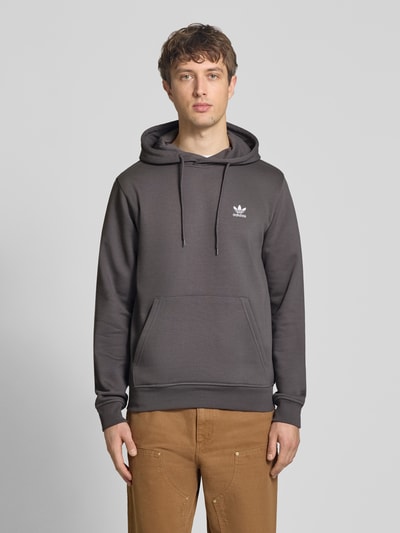 Männermodel trägt Regular Fit Hoodie aus Baumwoll-Mix von adidas Originals in Dunkelgrau mit Logo-Stitching, Sweat-Material, Ganzkörperansicht von vorne.
