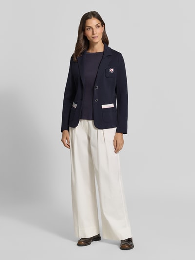 Vrouwenmodel draagt Regular Fit Blazer met Reverskraag van Marc Cain, donkerblauw katoenmix met stretch, opgestikte zakken, borstzak met bloemenapplicatie, knoopsluiting, ruglengte maat 36: 59 cm, borstwijdte 47 cm, mouwlengte 63 cm, vooraanzicht volledig lichaam.