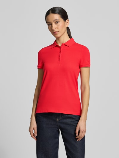 Frauenmodel trägt Slim Fit Poloshirt mit Knopfleiste von Christian Berg Woman, leuchtend rot, glatte Textur, Baumwoll-Elasthan-Mix, Seitenschlitze, Rückenlänge bei Größe S 62 cm, Ganzkörperansicht von vorne.