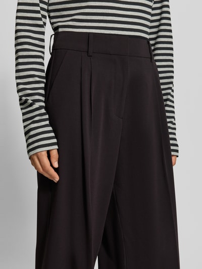 Frauenmodel trägt Wide Fit Hose mit Viskose-Anteil von MYON, Bundfalten, elastischer Material-Mix, dunkle Farbe, Nahaufnahme Oberkörper.