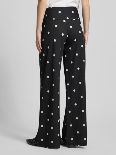 Vrouwenmodel draagt Wide Leg Pants aus Viskose-Mix mit seitlichem Reißverschluss van Gina Tricot met polkadots, zwarte stof met witte stippen, wide fit model, bandwijdte bij maat S 41 cm, binnenbeenlengte 82 cm, ganzkörperansicht rückansicht.