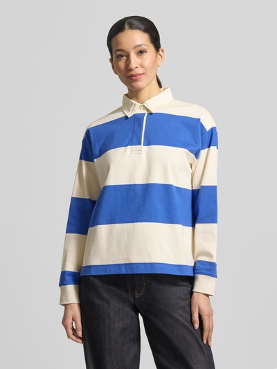 Frauenmodel trägt Regular Fit Langarm-Poloshirt mit verdeckter Knopfleiste von Gant, Baumwolle, Polokragen, in Creme und Blau, Ganzkörperansicht von vorne.