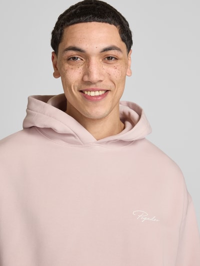 Männermodel trägt Oversized Hoodie mit Känguru-Tasche Modell 'Pike' von Pegador aus Baumwoll-Mix mit Label-Print, Nahaufnahme Oberkörper.