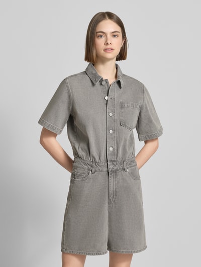 Frauenmodel trägt Regular Fit Playsuit in Denim-Optik Modell 'Fillipa' von JJXX aus Reine Baumwolle mit Knopfleiste, Kurzärmelig, Umlegekragen, Brusttasche und 5-Pocket-Design, graue Farbe, glatte Textur, Ganzkörperansicht von vorne.
