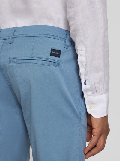 Männermodel trägt Slim Fit Chinoshorts aus Baumwoll-Mix von Tom Tailor, efekt: wzór na całej powierzchni, krój slim fit, tkany wzór, aplikacja z logo, szlufki na pasek, zapięcie na guzik i ukryty zamek błyskawiczny, wpuszczane kieszenie, kieszenie z tyłu, wykończenie materiału: splot twill, mieszanka bawełny, detal: jasnoniebieski, gładka tekstura. Detailaufnahme Rückansicht.