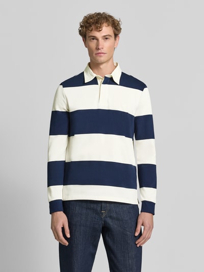 Männermodel trägt Poloshirt aus reiner Baumwolle von Christian Berg Men, weite Streifen in Dunkelblau und Creme, lockere Passform, Ganzkörperansicht von vorne