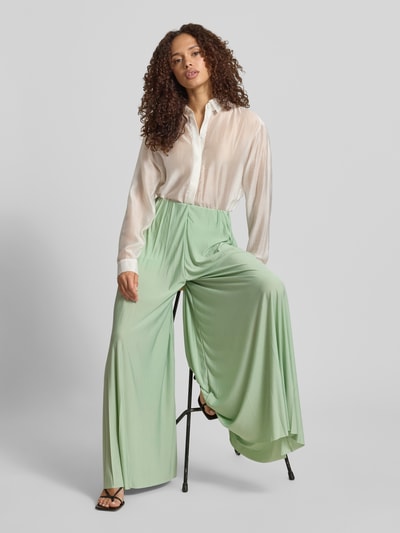 Vrouwenmodel draagt stoffen broek van satijn, wide leg fit, model 'Samantha' van GUIDO MARIA KRETSCHMER WOMAN, plissévouwen, elastische band, lichtgroen, gladde textuur, bandwijdte maat 36: 34 cm, binnenbeenlengte maat 36: 73 cm. Ganzkörperansicht von vorne.