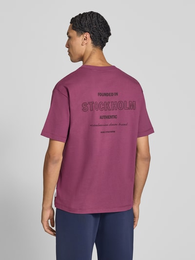Männermodel trägt Relaxed Fit T-Shirt aus reiner Baumwolle von Marc O'Polo DENIM in Dunkelviolett mit schwarzem Aufdruck, Ganzkörperansicht Rückansicht.
