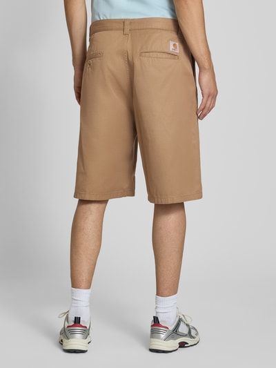 Männermodel trägt Bermudas mit Baumwoll-Anteil Modell 'Brader' von Carhartt Work In Progress in Beige mit Gesäßtaschen, Ganzkörperansicht Rückansicht. Material-Mix, Relaxed Fit, Bundweite 44 cm, Innenbeinlänge 30 cm, Knopf- und Reißverschluss, Gürtelschlaufen.