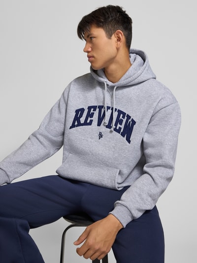 Männermodel trägt Hoodie mit Label-Stitching von REVIEW in Hellgrau, Baumwollmischung, lockere Passform, Nahaufnahme Oberkörper.