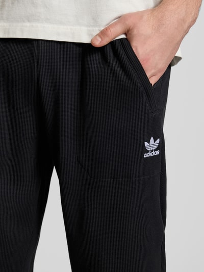 Männermodel trägt Straight Fit Sweatpants mit elastischem Bund Modell 'Essentials' von adidas Originals, schwarzer Strukturstoff, Nahaufnahme Oberkörper.