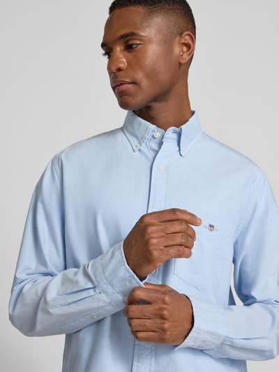 Męski model nosi Regular Fit koszulę casualową z bawełny model 'OXFORD' od GANT, jednokolorowy niebieski, z kołnierzykiem typu button down i brustaszą, wyhaftowane logo, widok na górną część ciała z przodu. Długość tyłu 79 cm, szerokość ramion 43 cm, długość rękawa 66 cm.