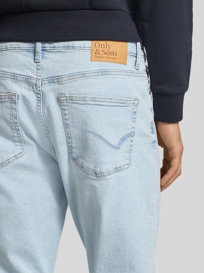 Männermodel trägt Slim Fit Jeans aus Baumwoll-Mix Modell 'WEFT' von Only & Sons in heller Denim-Optik mit Label-Patch, Detailaufnahme Rückansicht.