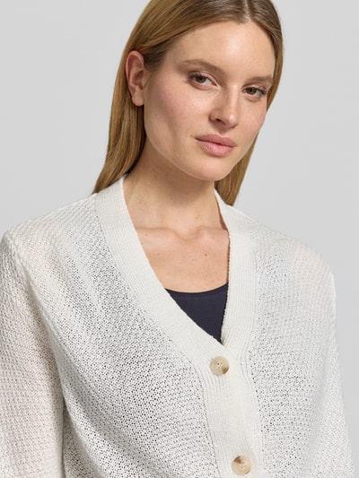 Modelka kobieca ma na sobie kardigan mit V-Ausschnitt und 3/4-Arm von More & More w kolorze jasnym, listwa guzikowa, krój relaxed fit, dekolt w serek, długość tyłu w rozmiarze 36 to 48 cm, długość rękawów w rozmiarze 36 to 24 cm, widok z przodu, zbliżenie na górną część ciała.